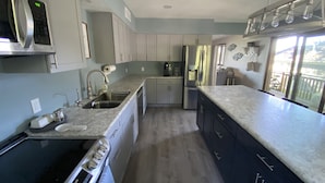 Una cocina moderna con electrodomésticos de acero inoxidable, encimera de granito y vistas al exterior a través de amplios ventanales.