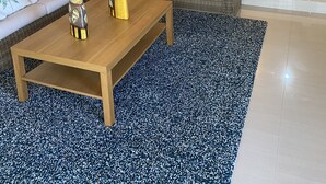 Een woonkamer met een bank, een bijzettafeltje en een eethoek met rieten meubels.