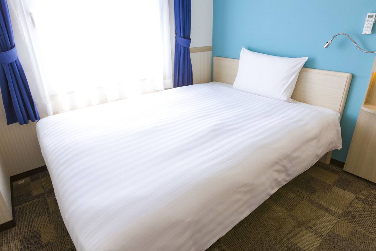 Een keurig opgemaakt bed in een hotelkamer, met een blauwe muur en een nachtkastje met een lamp.