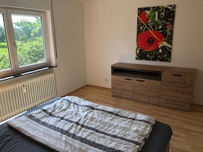 Ein Schlafzimmer mit Bett, Heizkörper, Fenster und Holzschrank.