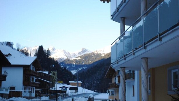 A snow-covered street with traditional wooden houses and a modern building with balconies. - Apartment 'Bergglück' with Mountain View, Balcony and Wi-Fi (See)