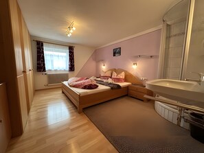 Ein Schlafzimmer mit Bett, Nachttischen, einem großen Fenster, einer Heizung und einem Badezimmer mit Waschbecken und Spiegel.