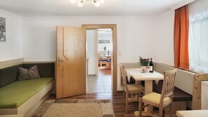 A room with a wooden door, a green sofa, a dining table with chairs, and a window with curtains. - Apartment 'Bergglück' with Mountain View, Balcony and Wi-Fi (See)