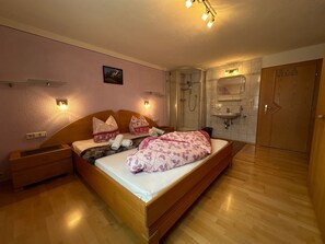 A bedroom with a wooden bed, bedside tables, a shower, a sink, and a door. - Apartment "Bergglück" with Mountain View, Wi-Fi & Balcony (See)