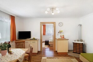 A compact living space with a dining area, a TV, a bed, a small kitchenette, and a radiator. - Apartment "Bergglück" with Mountain View, Wi-Fi & Balcony (See)