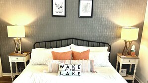 Een net opgemaakt bed met een kussen waarop staat: 'Liever Wakker aan het Meer'.