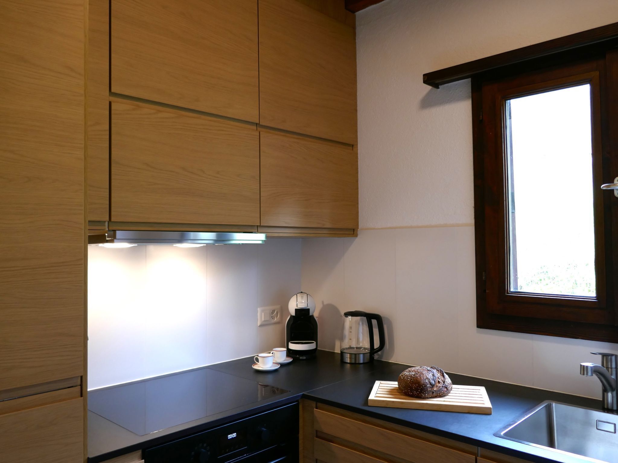 A modern kitchen with wooden cabinets, a black countertop, a window, and a stainless steel sink.