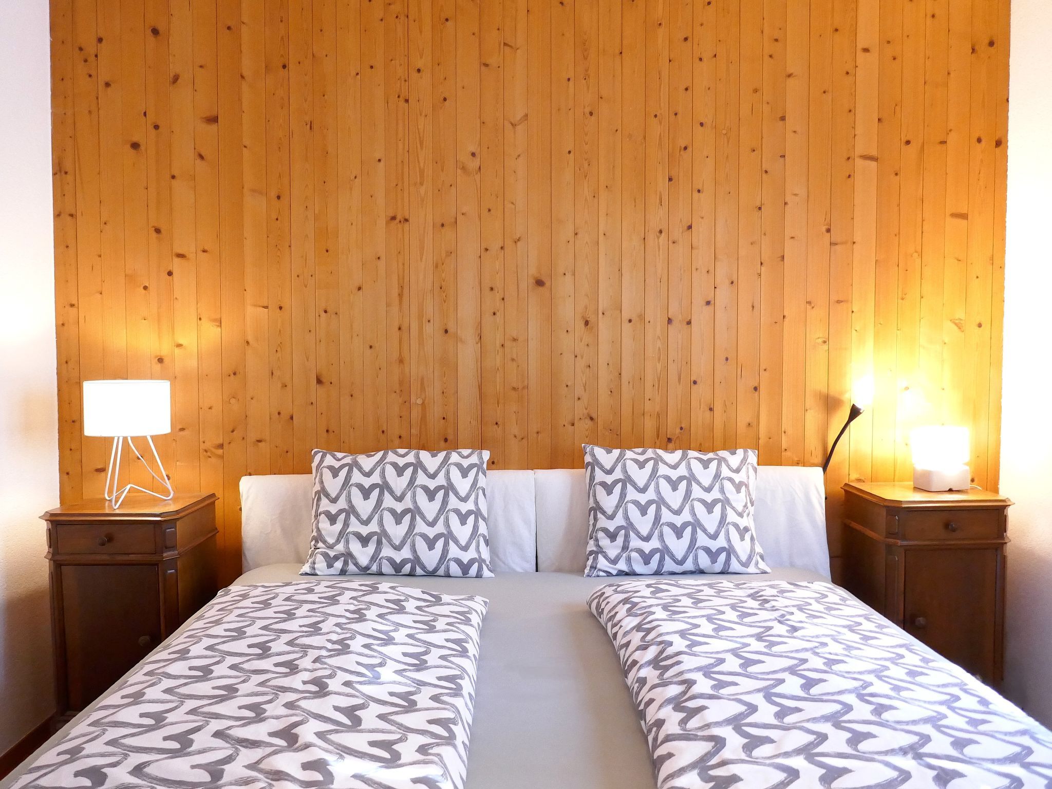 A double bed with patterned bedding, two bedside tables with lamps, and a wooden panel wall.