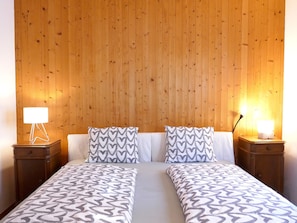 A double bed with patterned bedding, two bedside tables with lamps, and a wooden panel wall. - Chalet Al Portic by Interhome (Olivone)