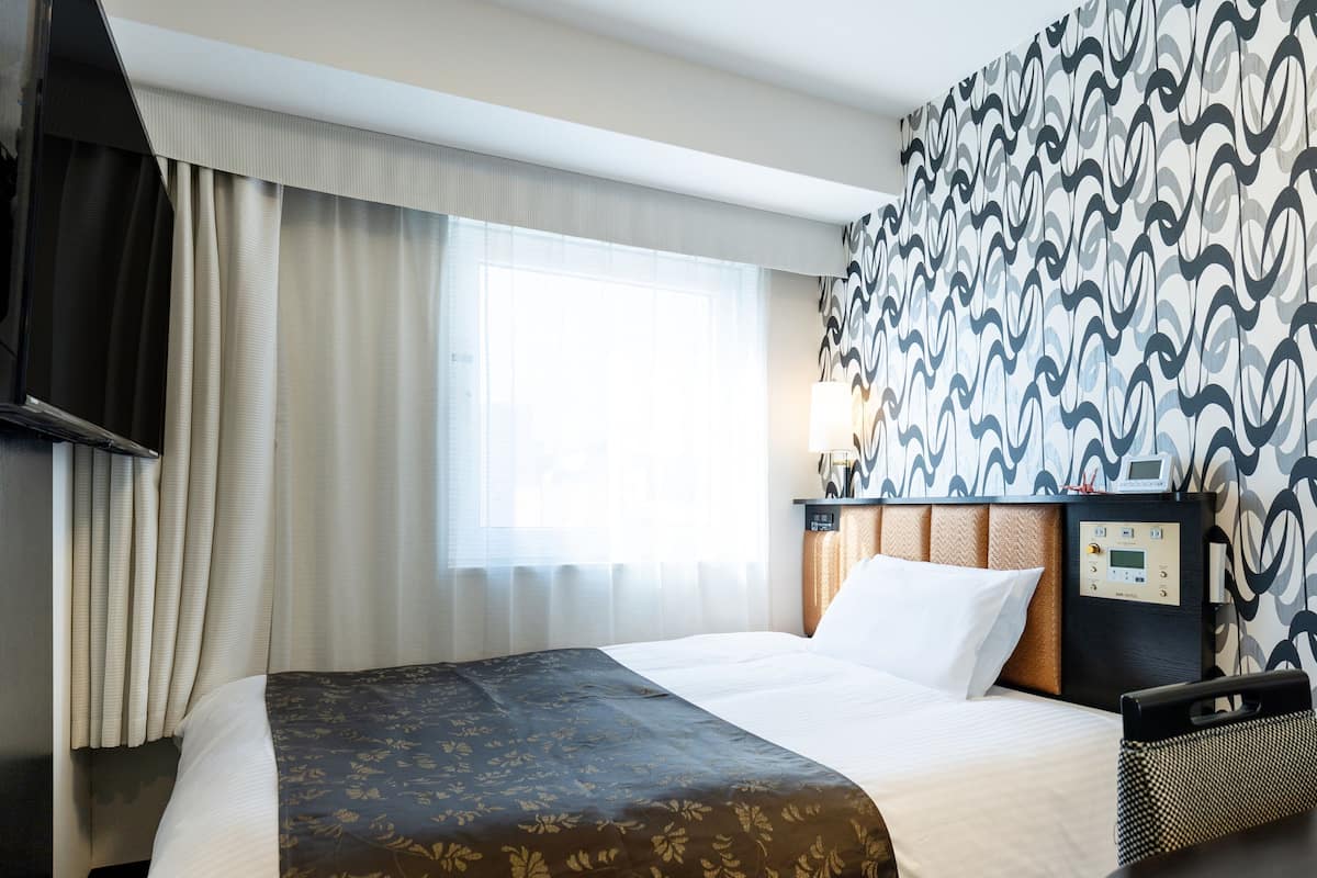 Une chambre d’hôtel équipée d’un lit, d’un bureau, d’une télévision et d’un panneau de commande.