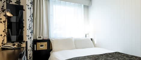 A hotel room with a bed, a desk with a lamp, a clock, and a window with curtains.