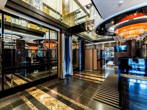 Een moderne hotelentree met een receptiebalie, zithoek en een kroonluchter.
