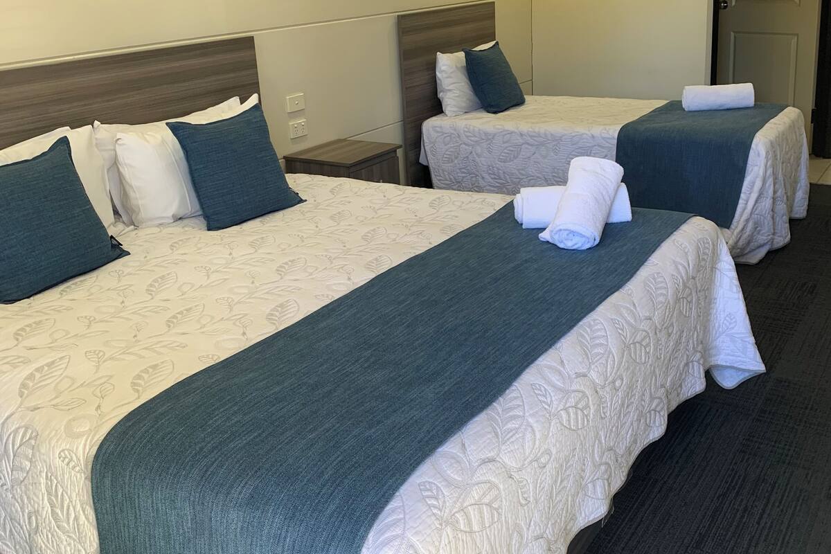 Habitación de hotel con dos camas, una mesita y un cuadro en la pared.
