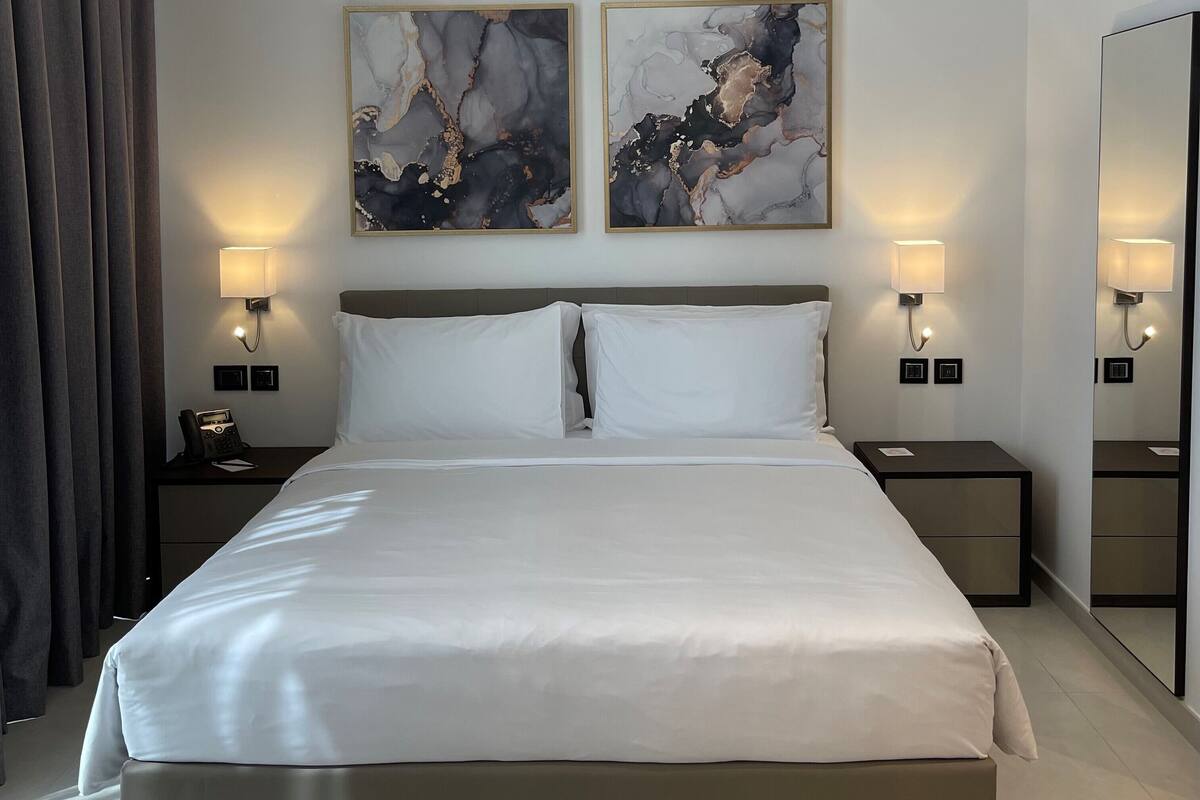 A modern hotel bedroom with a large bed, two bedside tables with lamps, and two abstract paintings on the wall.