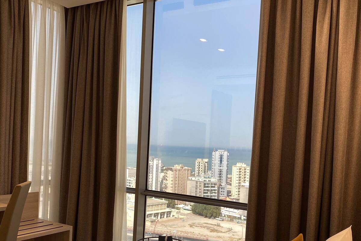 A hotel room with a large bed, a desk, and a view of a cityscape and water.
