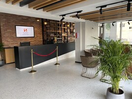 Zona de recepción de hotel con pared de ladrillo, mostrador negro y barrera de cuerda roja.