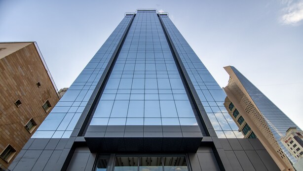 A tall, modern building with a glass facade and a brick base.