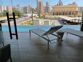 Un balcón con vistas a un paisaje urbano, una piscina y una mesa con una silla.