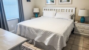 A neatly arranged bedroom with a bed, two bedside tables, a lamp, and two framed pictures on the wall. - Beautiful Ocean Views 2/2 Condo  (Orange Beach)