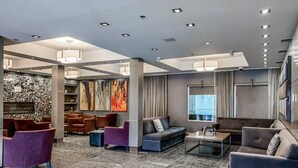 Een moderne lobby met een stenen muur, meerdere zithoeken en een groot raam met uitzicht.