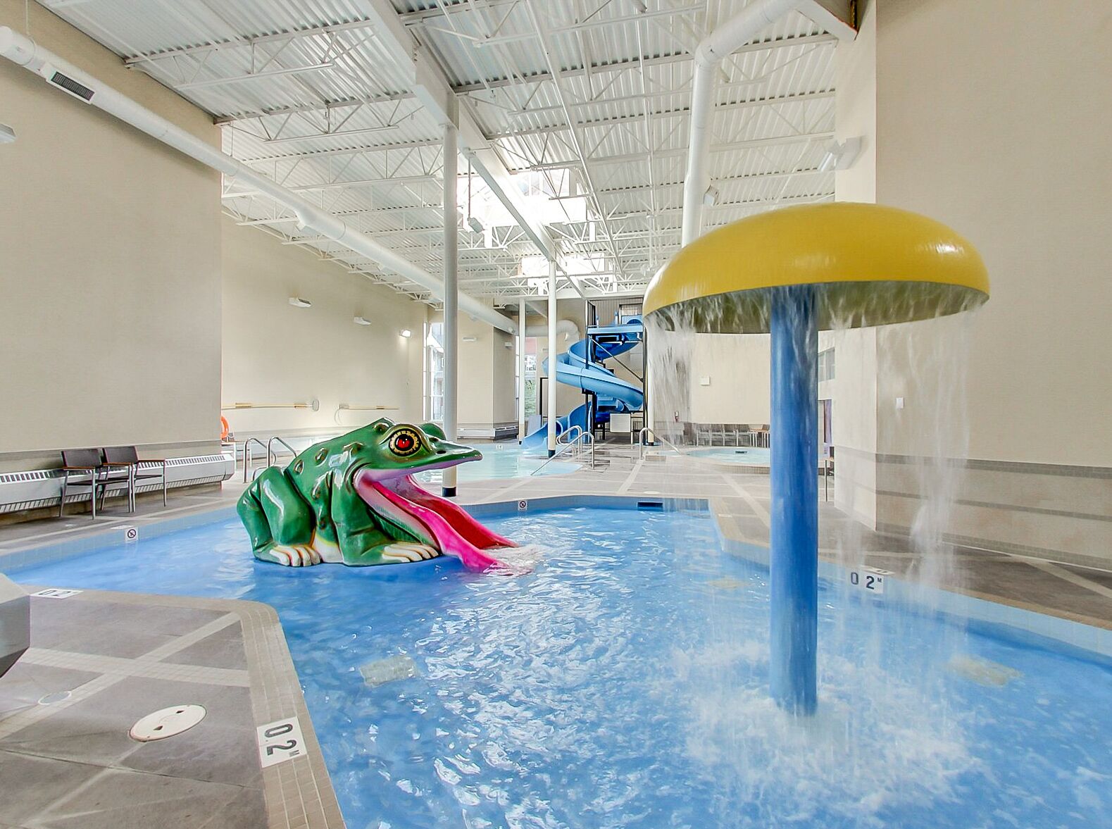 Un parc aquatique intérieur doté d’une grande sculpture de grenouille, d’un toboggan aquatique et d’un espace piscine.