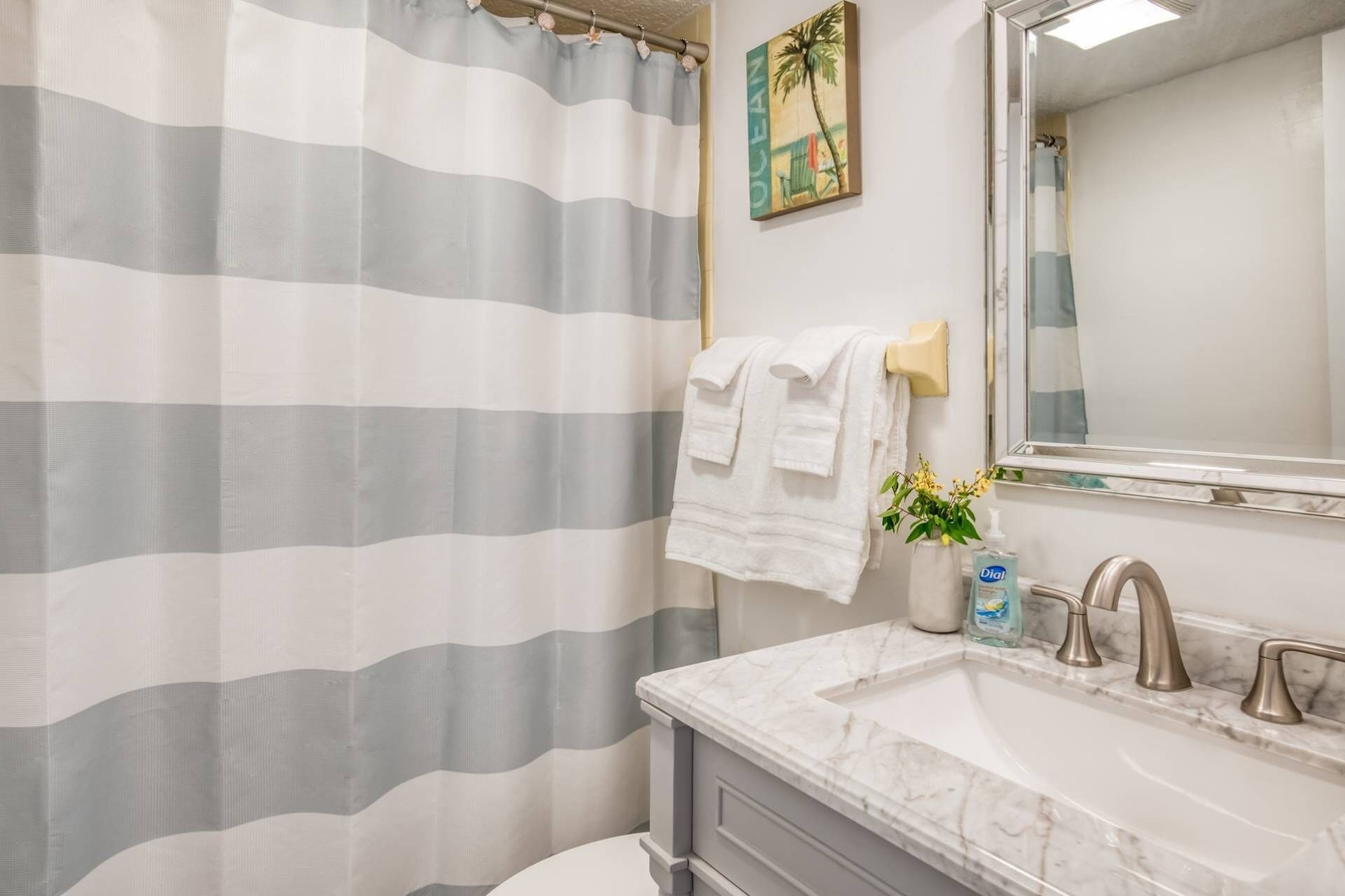 A bathroom with a striped shower curtain, a white towel hanging on the wall, a sink with a marble countertop, and a mirror above the sink.