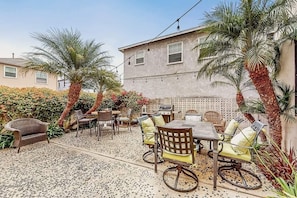 Eine Terrasse im Freien mit einem Esstisch und Stühlen, umgeben von Palmen und einer gemusterten Wand.
