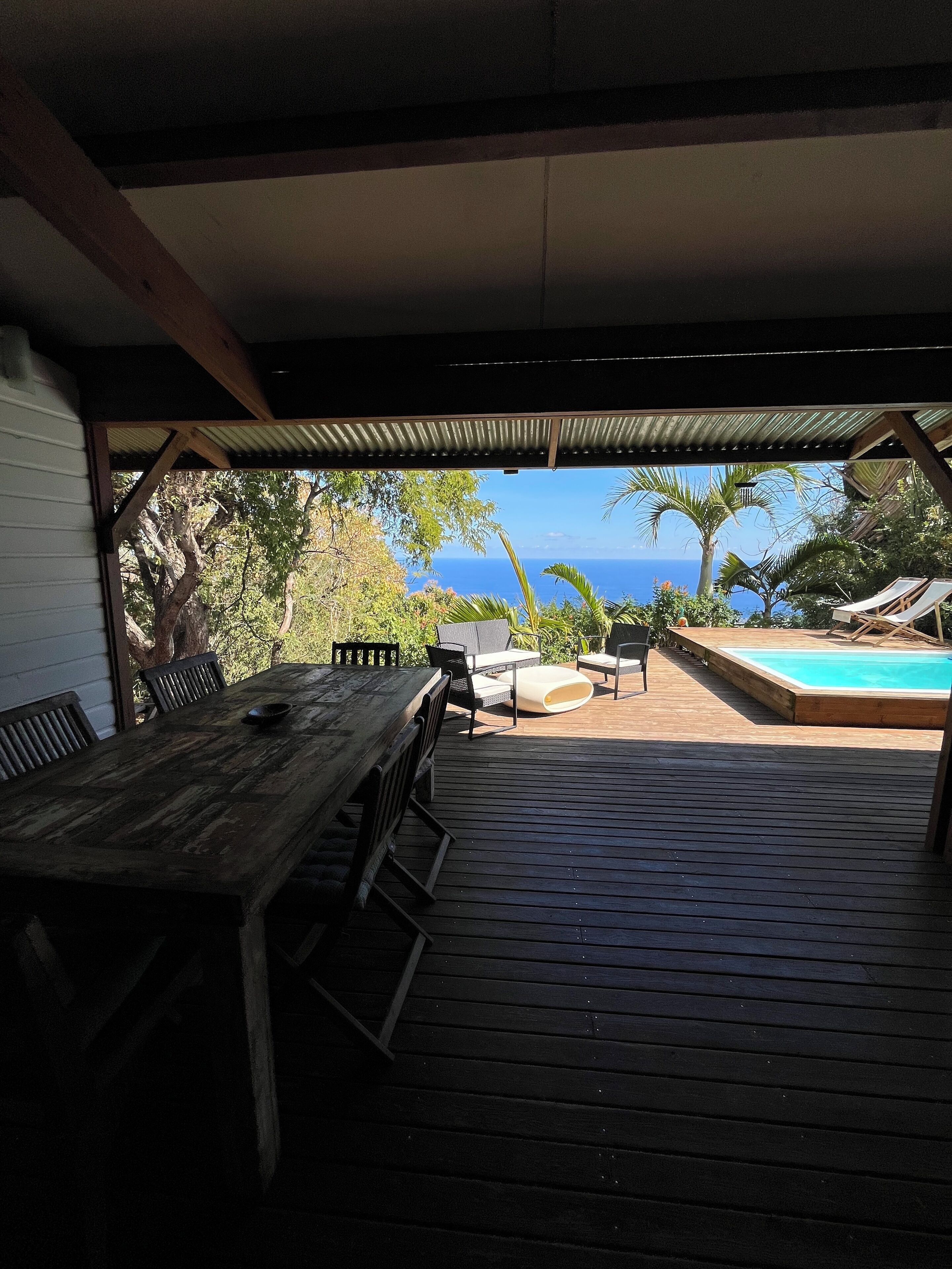 Una terraza de madera con piscina, mobiliario exterior y vista al océano.