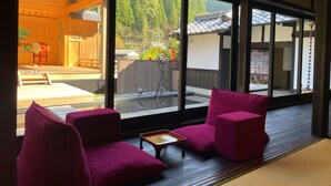 Een kamer met grote ramen, een houten vloer en twee roze stoelen.