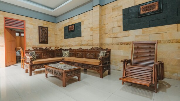 A spacious living area with a wooden sofa set, a coffee table, and a wooden chair. - Homestay Simply Homy Unit Gembiraloka (Yogyakarta)