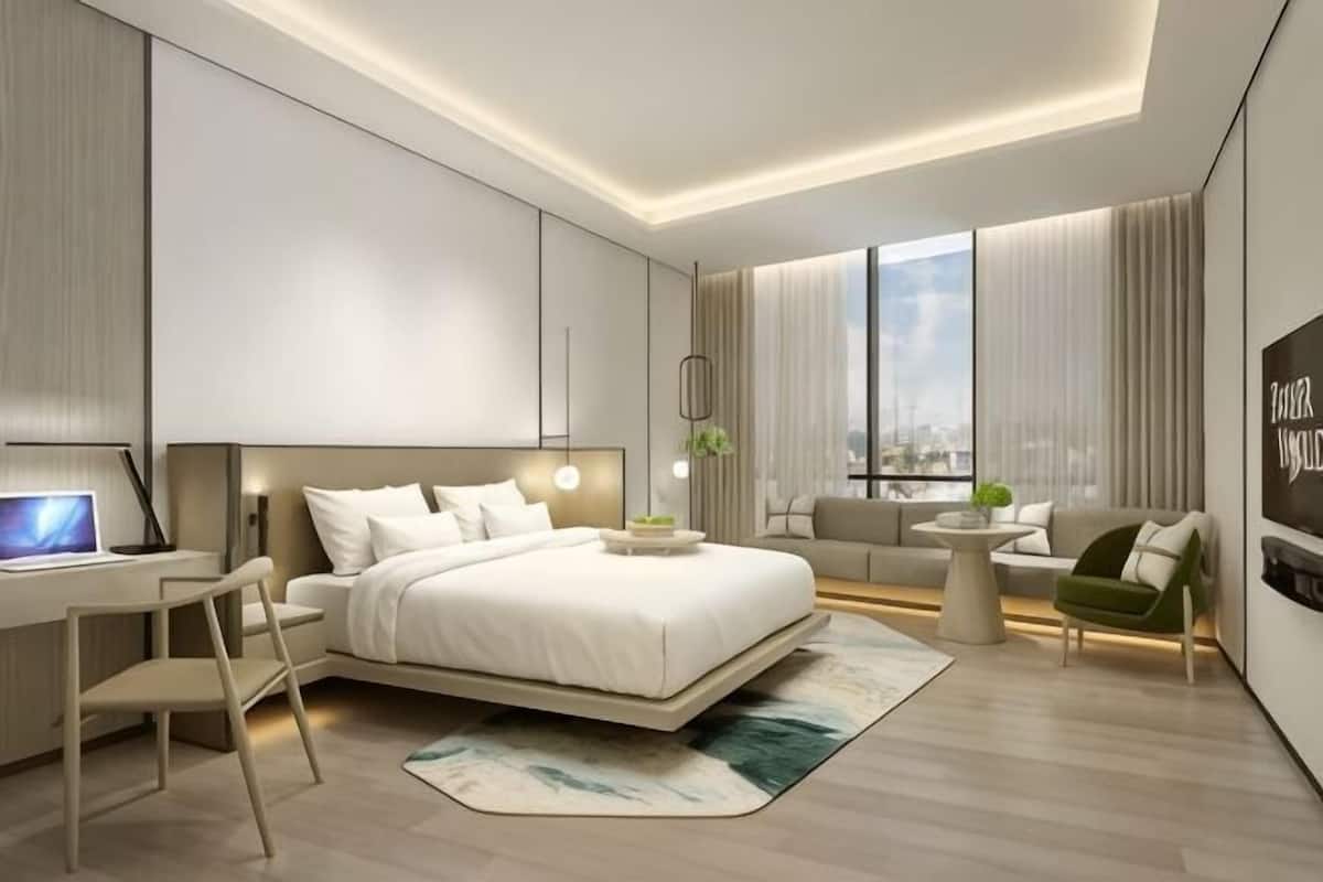 A modern hotel room with a bed, desk, and seating area.