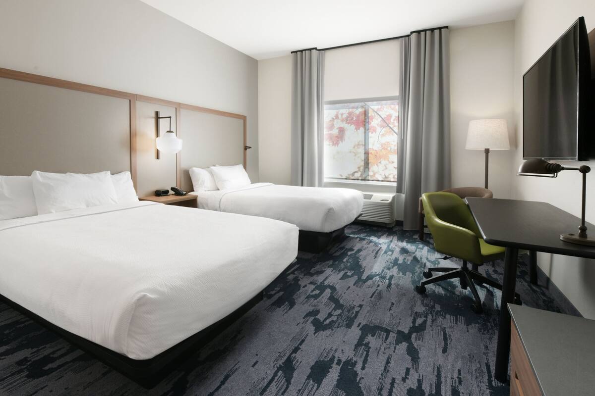 Een hotelkamer met twee bedden, een bureau, een stoel, een televisie en een raam met gordijnen.