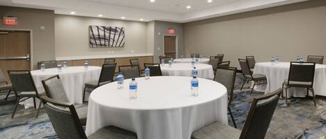 Un salón de conferencias con mesas redondas, sillas y botellas de agua.