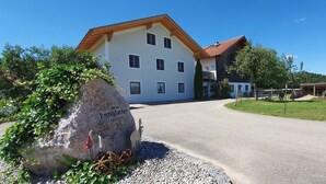 Un edificio a due piani con facciata bianca e tetto rosso, una pietra con iscrizioni e un vialetto sterrato.