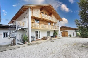 A two-story chalet with a balcony, a spiral staircase, and a gravel driveway.