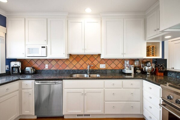A modern kitchen with white cabinets, a granite countertop, stainless steel appliances, and a backsplash with a diamond pattern.