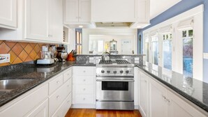Una cocina moderna con armarios blancos, estufa de acero inoxidable y encimera de granito negro.