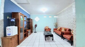 Een woonkamer met een bank, een bijzettafeltje, een waterdispenser en een boekenkast.