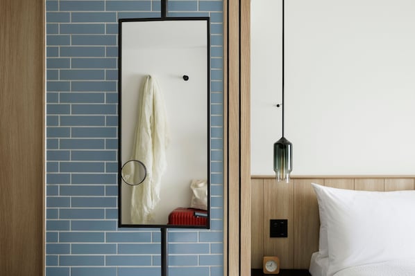 Habitación de hotel con pared de ladrillo azul, un espejo, una mesita de noche de madera, una maleta roja, un almohadón blanco y una lámpara colgante.