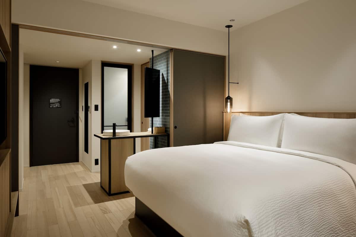 Een moderne hotelkamer met een groot bed, een nachtkastje, een spiegel en een klein bureau met een lamp.