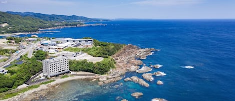 An aerial view of a coastal area with a hotel, rocky shoreline, and clear blue sea.