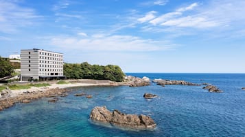 A coastal hotel with a modern design, situated near rocky waters and a clear sky.