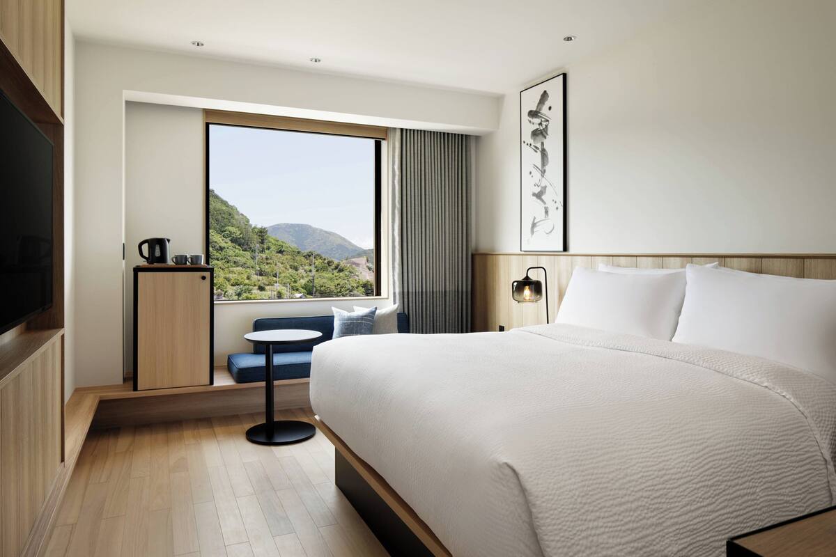 Een moderne hotelkamer met een groot bed, een zithoekje, een raam met uitzicht op groen en een flatscreen-televisie.