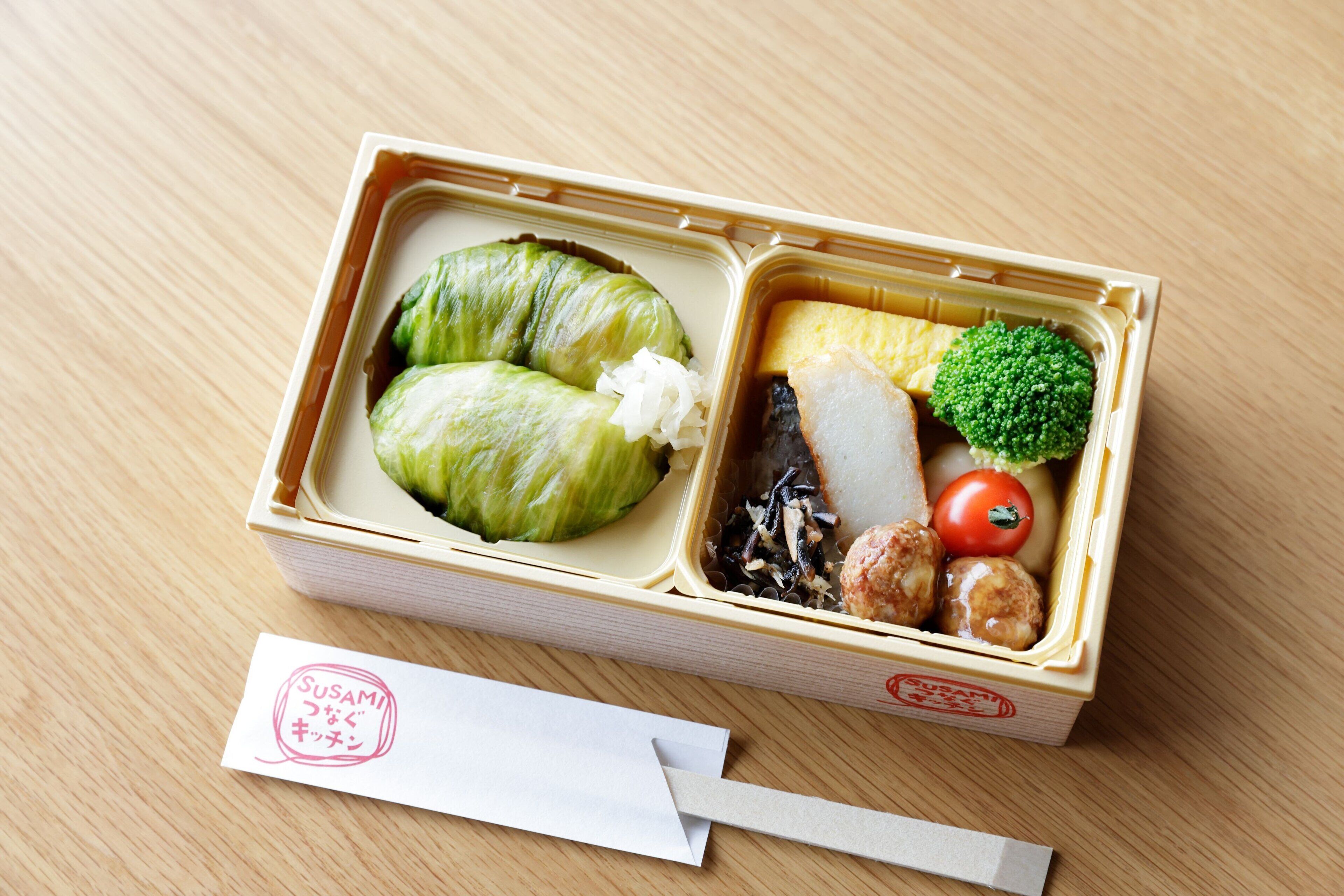 A bento box with various food items including sushi, vegetables, and a piece of fish.