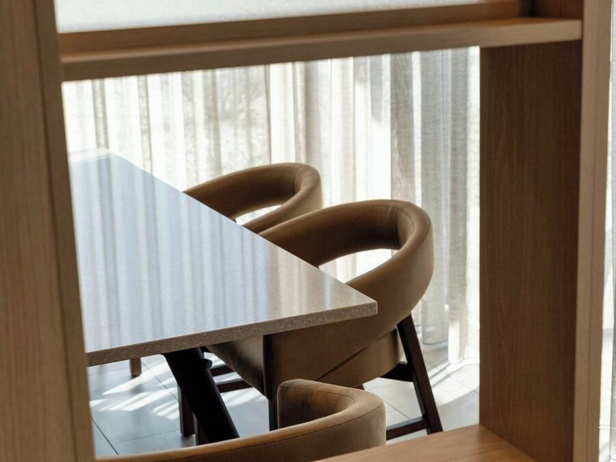 A dining area with a table and two chairs, a wooden shelf, and a frosted glass partition.