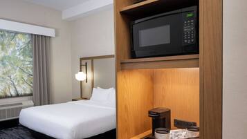 A hotel room with a bed, a microwave, a coffee maker, and a refrigerator.