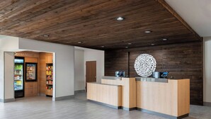 A reception area with a wooden reception desk, a corner market, and a decorative wall piece. - Fairfield Inn & Suites by Marriott Louisville Shepherdsville (Louisville)