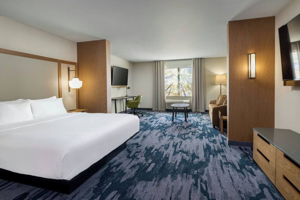 A hotel room with a large bed, a desk, a chair, a TV, and a window with curtains.