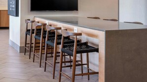 A modern bar area with a large flat-screen TV, wooden bar stools, and pendant lighting. - Fairfield Inn & Suites by Marriott Louisville Shepherdsville (Louisville)