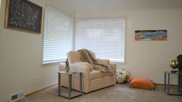 A living room with a beige sofa, a small table with a plant, a globe, and a painting of a landscape. - Quiet Comfort- Adventures Start Here! (Idaho Falls)